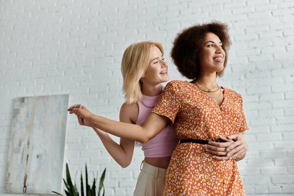 женщины, одна блондинка и одна с темными кудрявыми волосами, улыбайтесь и наслаждайтесь компанией друг друга в современной квартире