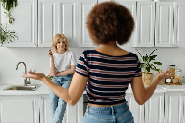 stock image Two women in a white kitchen, one blonde sitting and the other with curly brown hair standing with hands raised