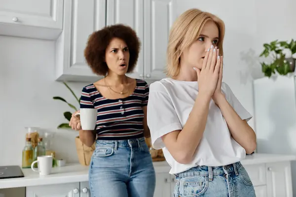 stock image Two women stand in a kitchen, one holding a mug, the other with hands over her mouth.