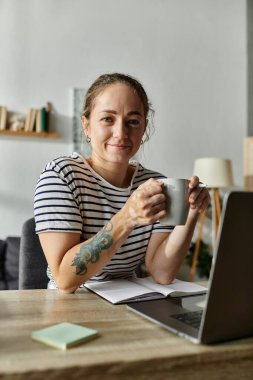 Genç bir kadın zarif çalışma alanında sıcak bir kupa tutarken gülümsüyor..