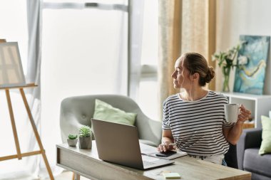 Bir kadın laptopuyla rahat bir ortamda çalışırken çaydan hoşlanır..