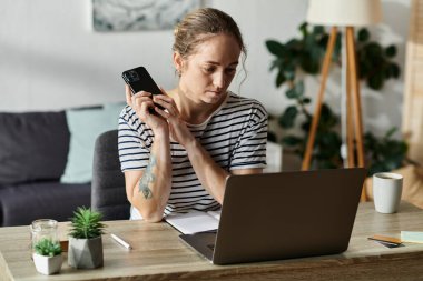 Genç bir kadın ahşap bir masada telefonunu kullanırken düşünür..