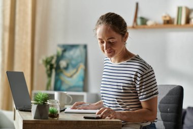 A young woman with vitiligo smiles while focusing on her work at a cozy desk. clipart