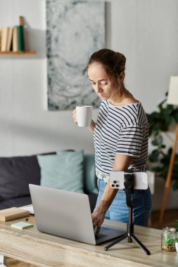 A woman with vitiligo focuses on her laptop while sipping coffee at her desk. clipart