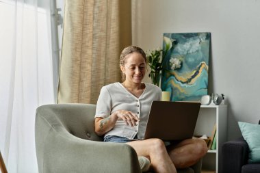 Gülümseyen kadın evde rahat otururken dizüstü bilgisayarıyla meşgul oluyor..