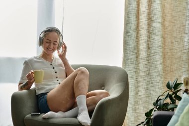 A woman with vitiligo smiles while sipping tea in a sunlit room. clipart