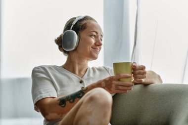 Vitiligo 'su olan bir kadın bir fincan çayla rahatlar, güneşli bir odada müzik dinler..