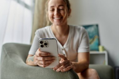 Vitiligo 'su olan bir kadın rahat bir kanepede telefonuna bakarken gülümsüyor..