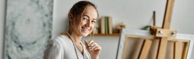 Vitiligo 'su olan bir kadın sanatsal çalışma alanında resim yaparken sıcak bir şekilde gülümsüyor..