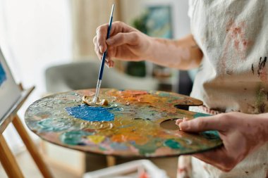 Genç bir sanatçı, stüdyosunda yaratırken ahşap bir palette renkleri harmanlıyor..