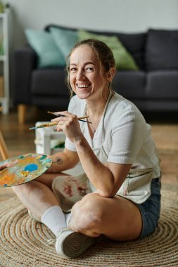 A talented woman with vitiligo smiles while painting in her artistic sanctuary. clipart