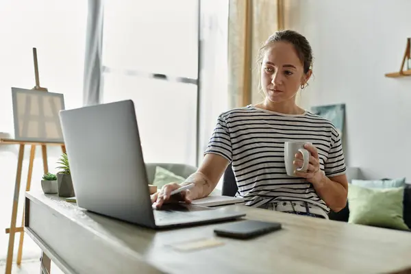 stock image A woman with vitiligo sips coffee while working on her laptop.