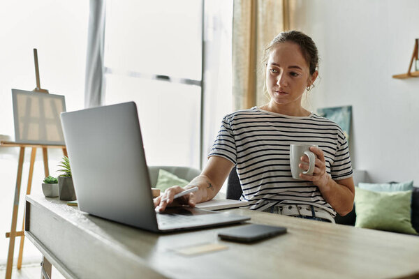 A woman with vitiligo sips coffee while working on her laptop.
