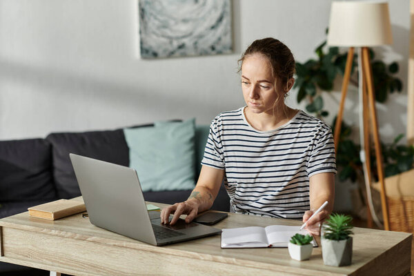 A beautiful woman with vitiligo writes in her notebook while focused on her laptop.