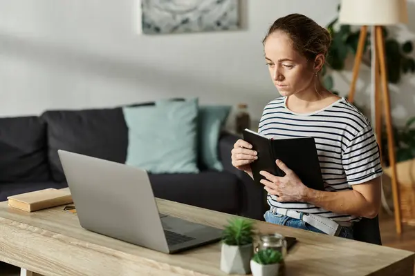 stock image A thoughtful woman with vitiligo holds a notebook, gazing at her laptop in a serene setting.