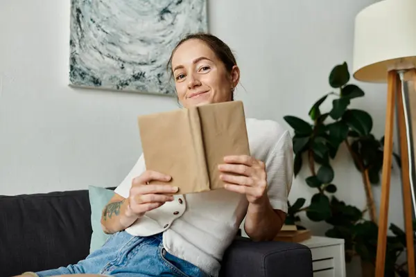 stock image A young woman smiles while reading a book in a warm, inviting space.