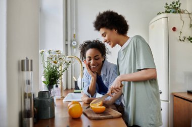 A loving couple shares smiles while preparing food in their inviting kitchen. clipart