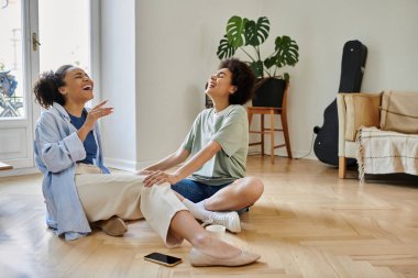 Two women share laughter and love in their cozy living room together. clipart