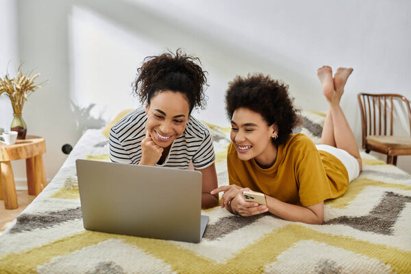 Две женщины наслаждаются компанией друг друга, наблюдая что-то смешное на ноутбуке.