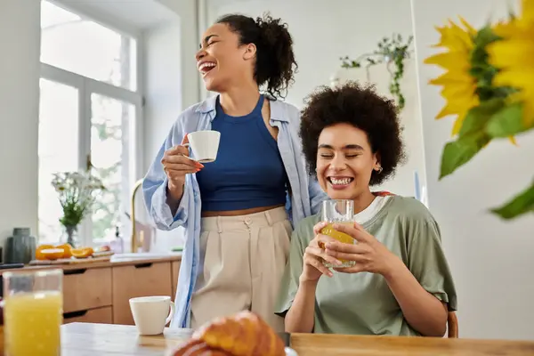 stock image Two women share laughter and drinks in a warm, inviting kitchen space.