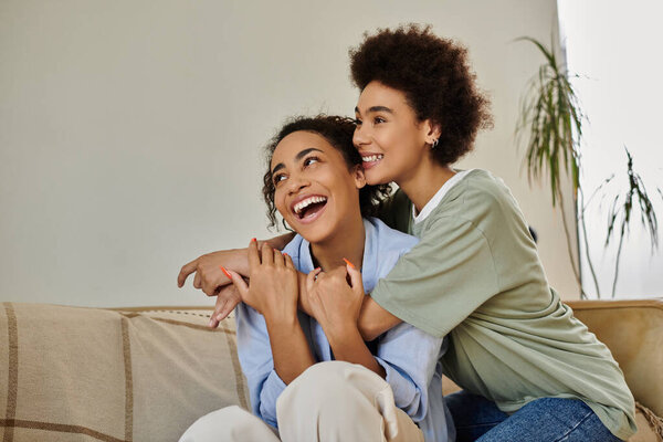 Две женщины разделяют смех и тепло, расслабляясь на диване.