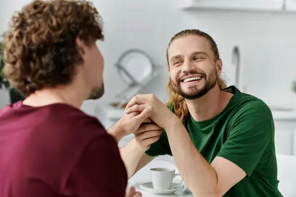 stock image Two men enjoy a warm moment together, holding hands and laughing in their cozy kitchen.