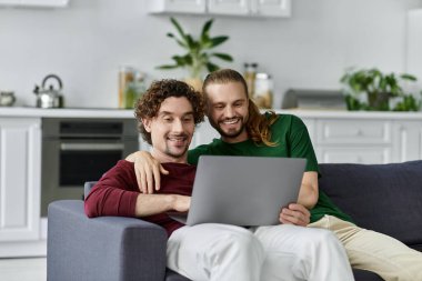 Two partners share laughter while browsing on a laptop at home. clipart