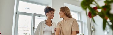 Two women share joyful moments in a cozy, bright space filled with plants. clipart