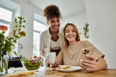 İki arkadaş kahvaltının ve sıcak içeceğin tadını çıkarırken kahkahalarını paylaşıyor..