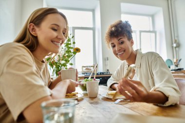 Güneşli bir mutfakta iki ortak kahkaha ve lezzetli yemekleri paylaşıyor..