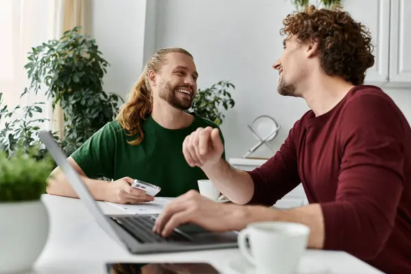 stock image Two men share laughter and love over coffee at their kitchen table.