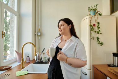 Kendinden emin bir kadın pencereden dışarı bakarken kahvesinin tadını çıkarıyor..