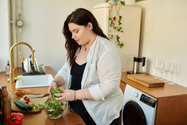 A woman lovingly assembles a vibrant salad with fresh ingredients at home.