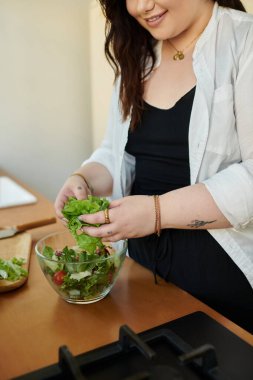 Neşeli, iri yarı bir kadın sıcak mutfağında canlı bir salata yapıyor..