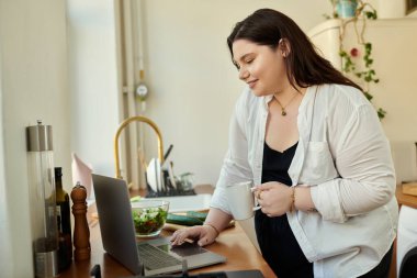 Neşeli bir kadın evinde dizüstü bilgisayarıyla çalışırken içkinin keyfini çıkarıyor..