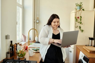 A plus size woman engages with her laptop while enjoying her kitchen. clipart