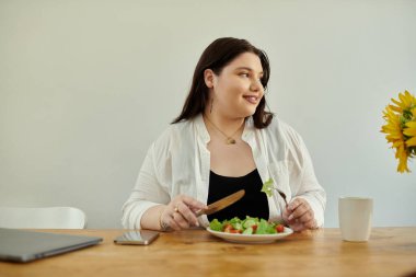 Büyük beden bir kadın yemek masasında canlı salatanın tadını çıkarırken gülümser..