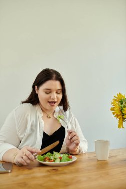 Tahta bir yemek masasında oturmuş salatanın tadını çıkarıyorum..