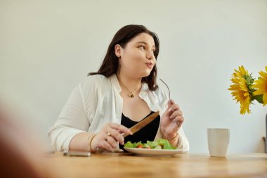 A woman savors a vibrant salad while seated at her cozy dining table. clipart