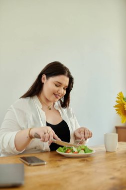 Bir kadın mutfak masasında otururken taze salatanın tadını çıkarır..