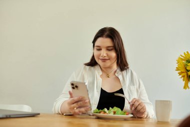 Güzel, iri yarı bir kadın telefonuna bakarken öğle yemeğinden zevk alır..