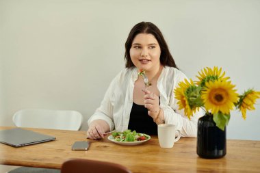 A joyful woman savors a healthy salad while surrounded by sunflowers. clipart