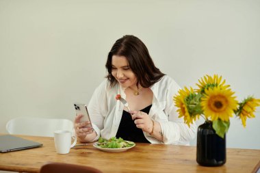 Bir kadın, taze ayçiçekleriyle çevrili telefonunu kontrol ederken yemeğinden zevk alır..