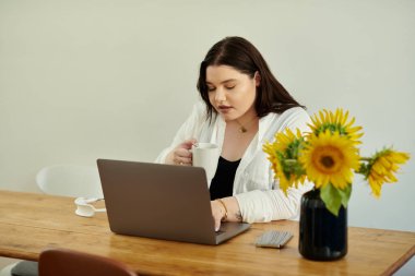 Büyük beden bir kadın, güneşli bir masada dizüstü bilgisayarıyla çalışırken sıcak bir içkiden hoşlanır..