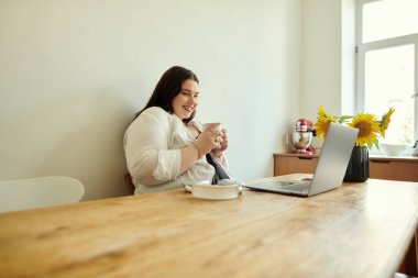 Büyük beden bir kadın evde kahve ve laptopuyla rahatlar..