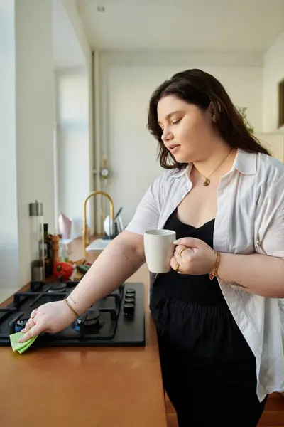 stock image A plus size woman savors coffee while tidying her kitchen space.