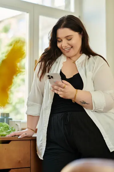 Stock image Plus size woman smiles as she checks her phone in her cozy home setting.