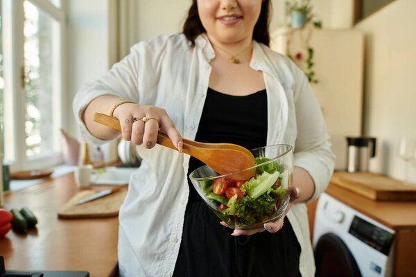A cheerful woman mixes fresh ingredients in a bowl while cooking.