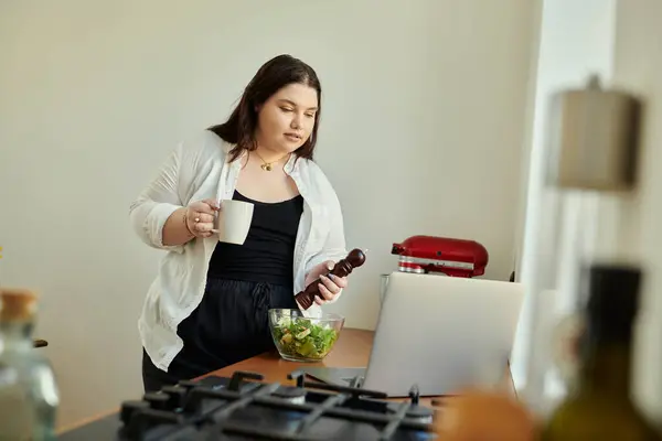 stock image A woman enjoys cooking a fresh salad while sipping coffee in her kitchen.