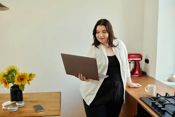 stock image A cheerful woman engaged with her laptop amid a bright kitchen.